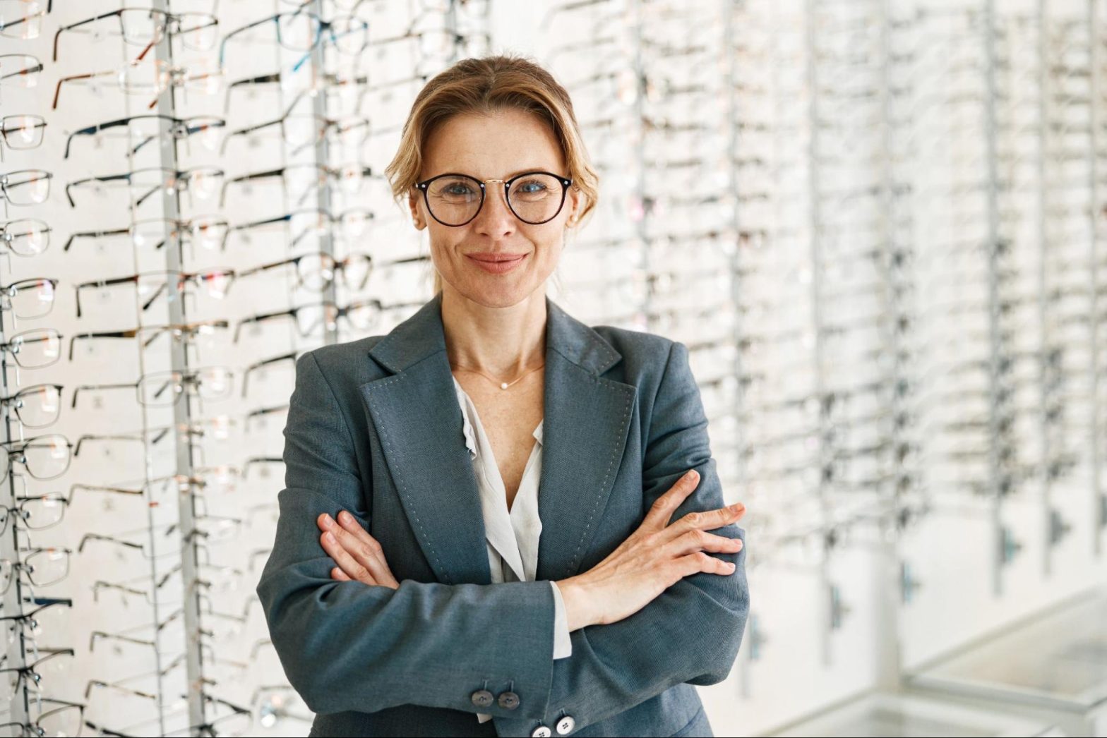 Proud, smiling optometrist standing in front of wall of eyeglasses